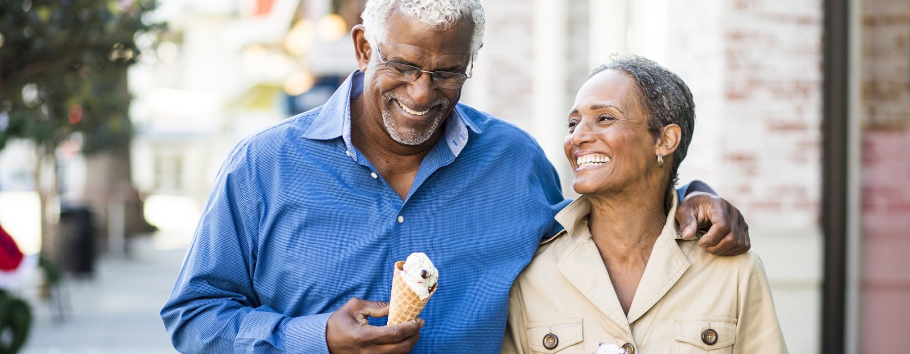 older couple walks down city sidewalk while holding ice cream cones